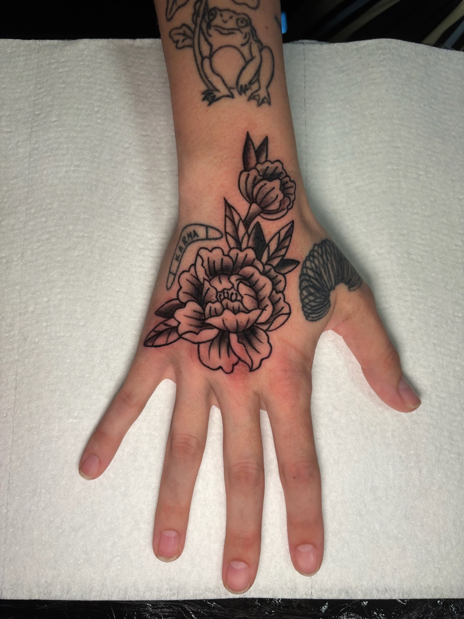 Hand tattoo with peony flowers and creature, neo-traditional