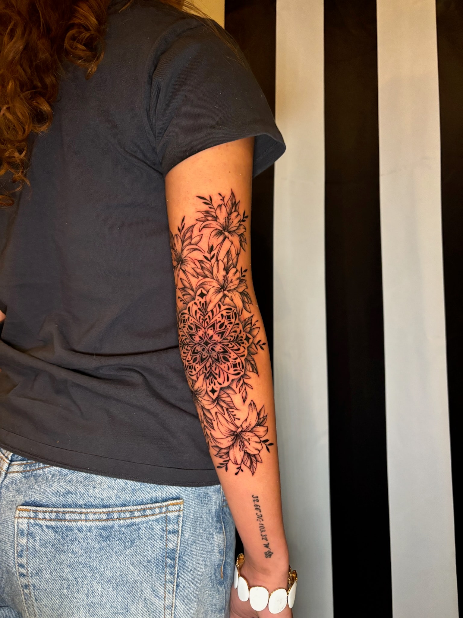 Floral mandala sleeve tattoo with lilies and coordinate script on forearm