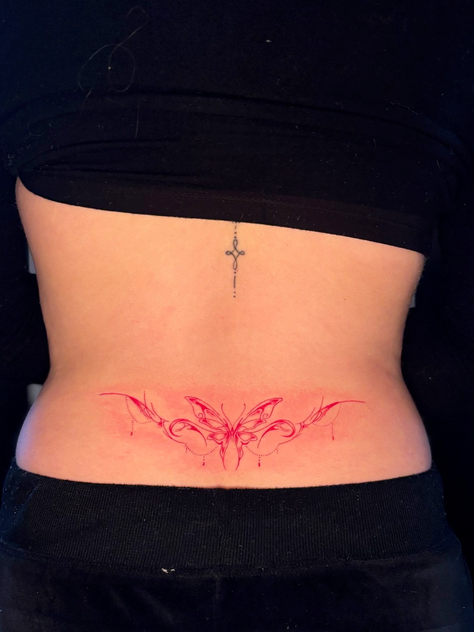 Red ink butterfly lower back tattoo with fine line cross spine tattoo above