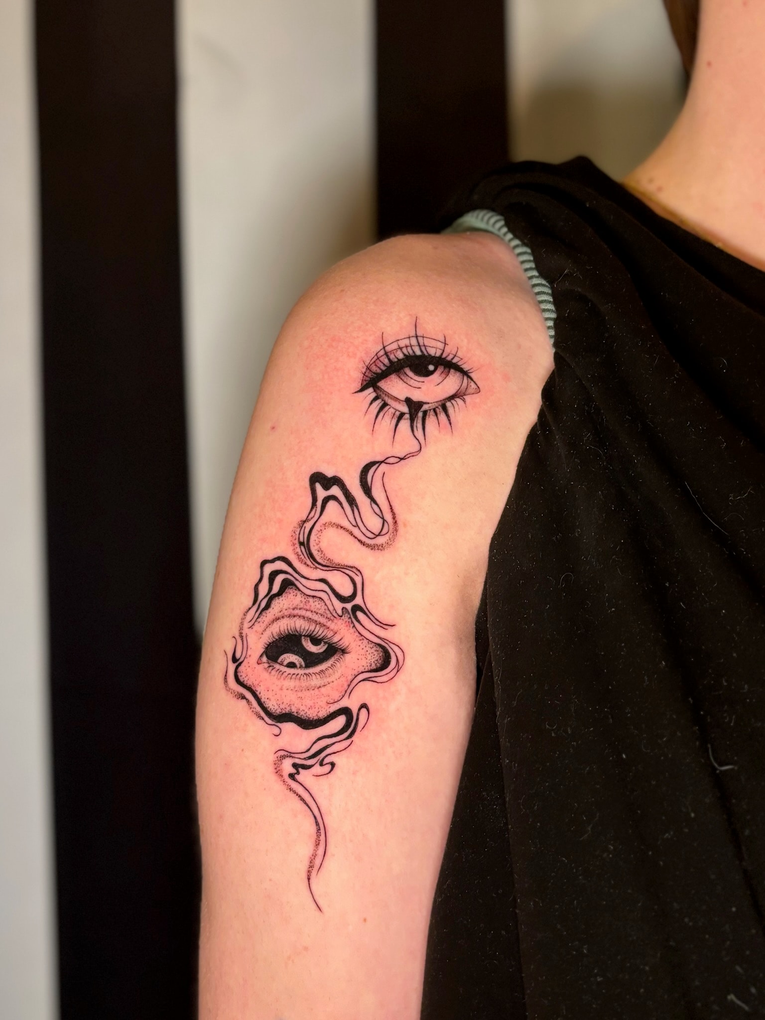 Surreal dual eye tattoo with organic flowing lines on upper arm, black and grey