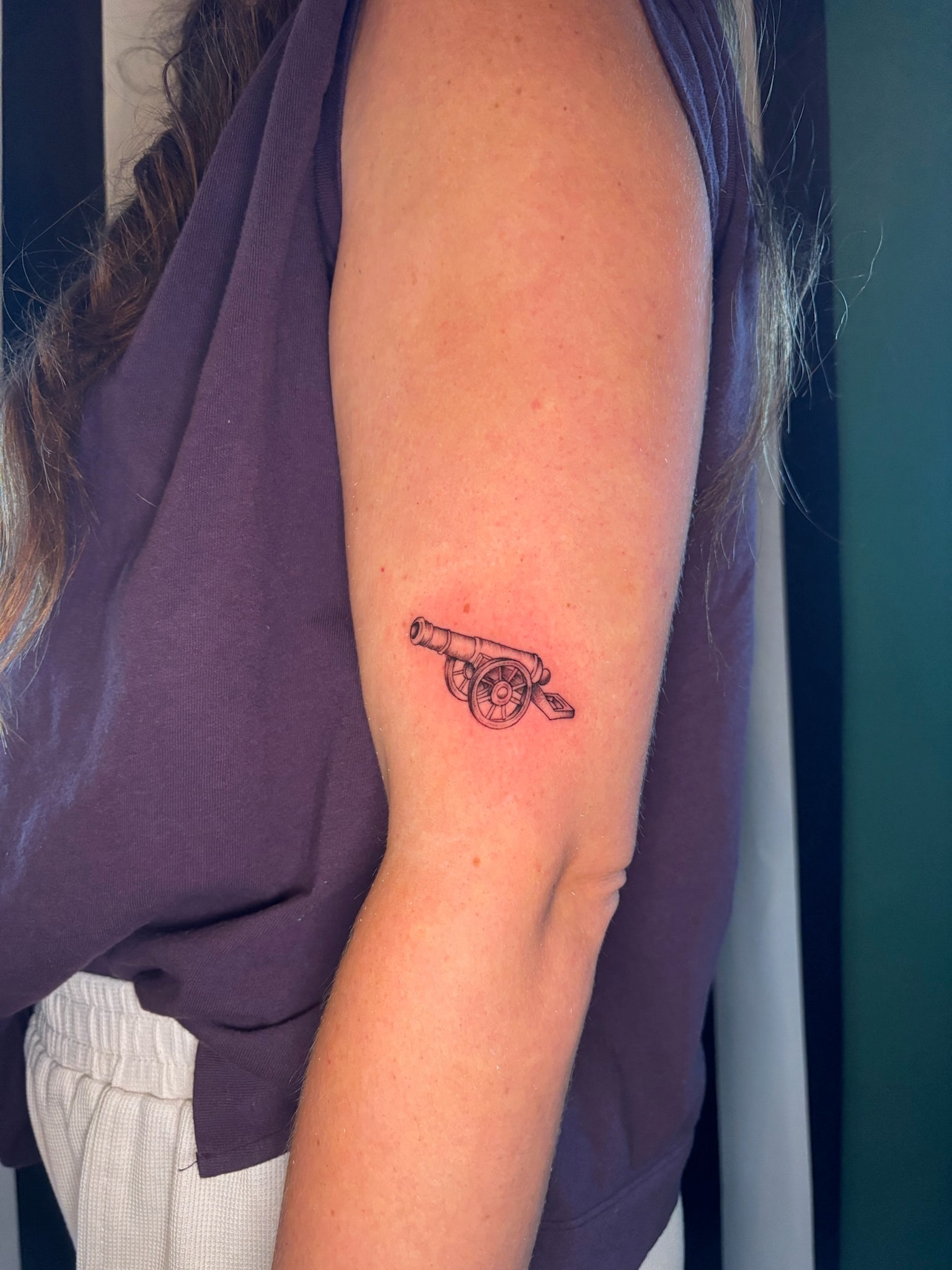 Small fine line cannon tattoo on upper arm