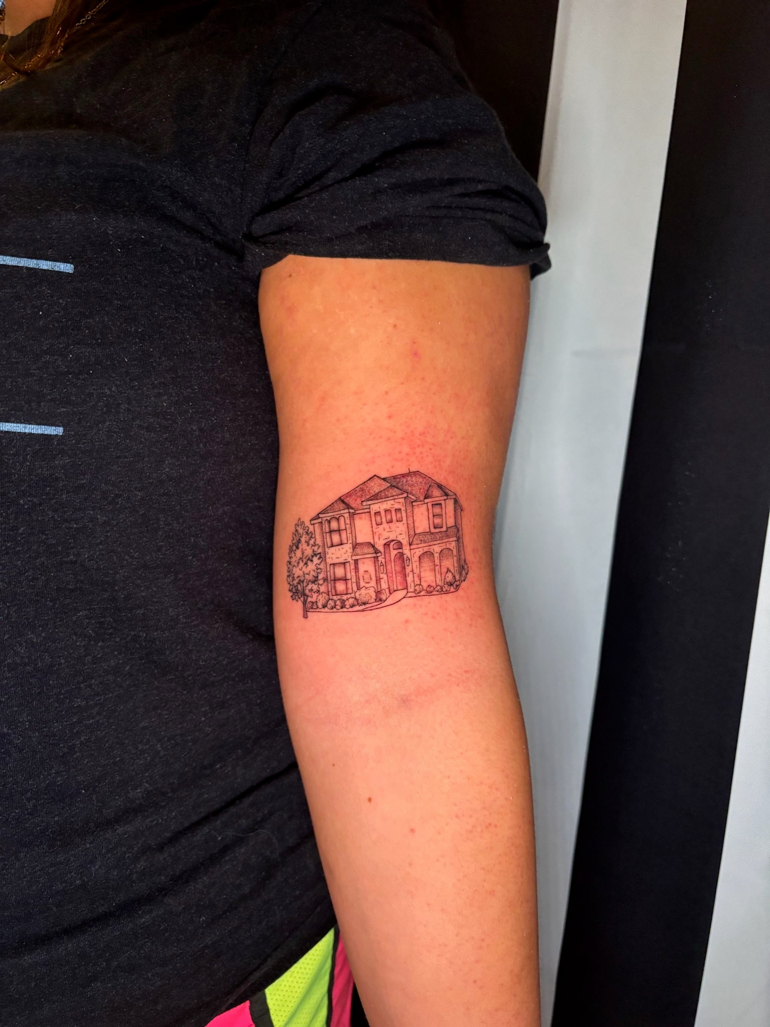 Fine line house portrait tattoo on upper arm with red roof and landscaping details