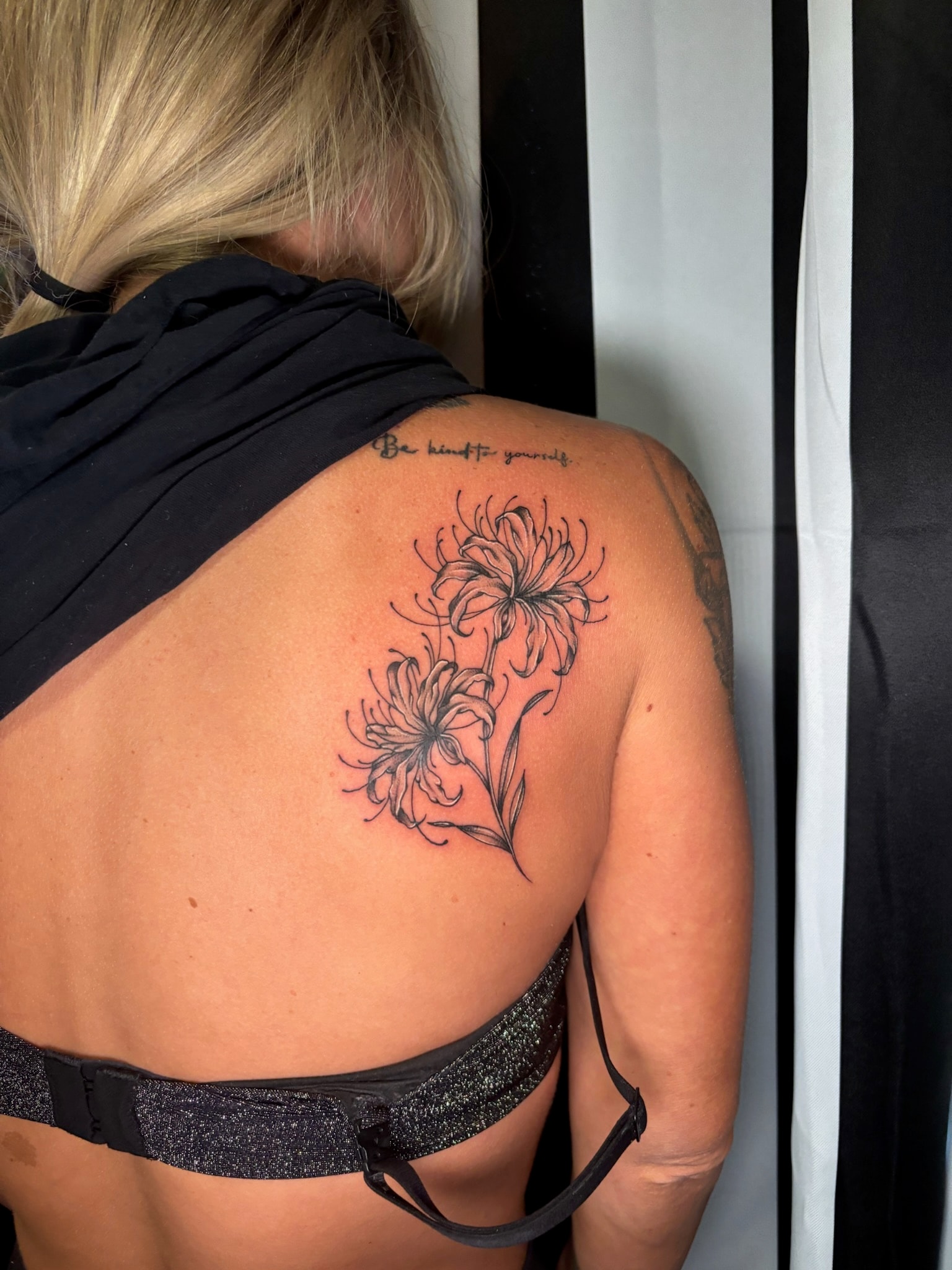 Fine line spider lily flowers back tattoo with Be kind to yourself script above