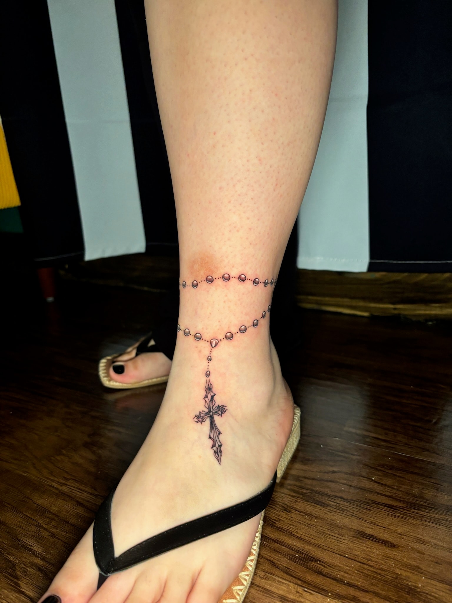 Rosary beads and cross tattoo on ankle, fine line